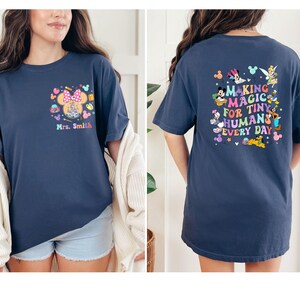 May include: Navy blue t-shirt with a Minnie Mouse design and the text "Mrs. Smith" on the front. The back of the shirt features Disney characters and the text "MAKING MAGIC FOR TINY HUMANS EVERY DAY."