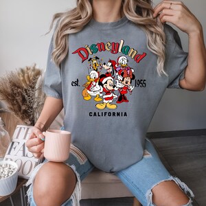 May include: Gray t-shirt with a graphic of Mickey Mouse and friends in front of a Disneyland sign that says "Disneyland est. 1955 California".