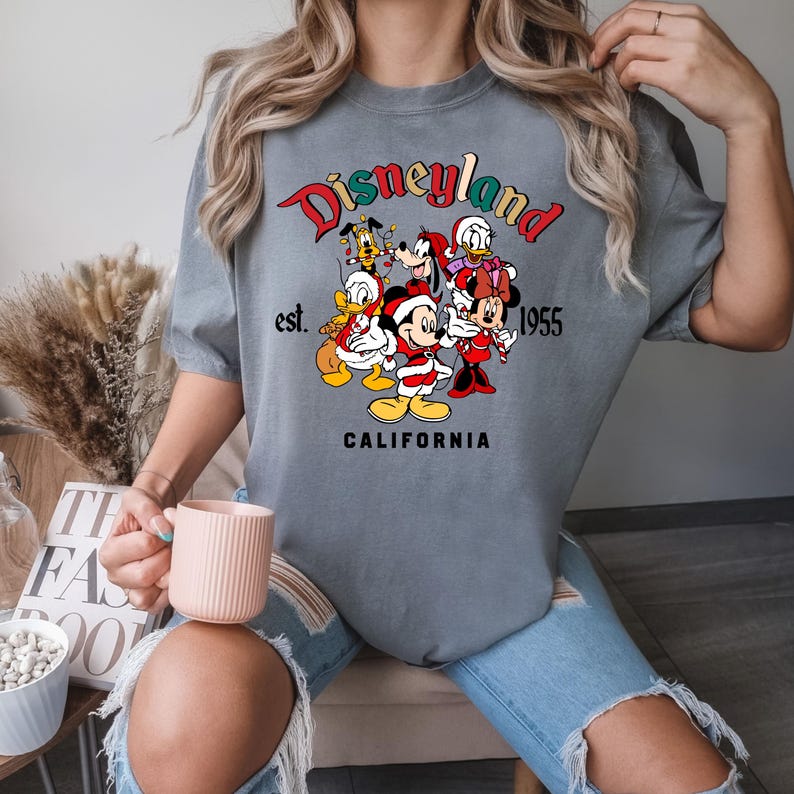 May include: Gray t-shirt with a graphic of Mickey Mouse and friends in front of a Disneyland sign that says "Disneyland est. 1955 California".