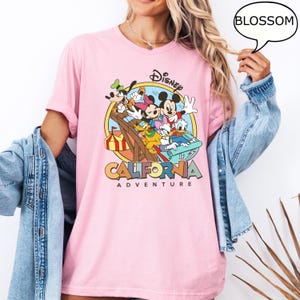 Puede incluir: Camiseta rosa con un gr&aacute;fico de Mickey Mouse y sus amigos montando una monta&ntilde;a rusa. El gr&aacute;fico est&aacute; rodeado de un c&iacute;rculo con el texto "Disney California Adventure" debajo.