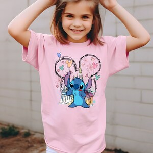 May include: A pink t-shirt with a blue Stitch character wearing Mickey Mouse ears with colorful balloons and fireworks. The shirt features a sketch of Cinderella's castle in the background.