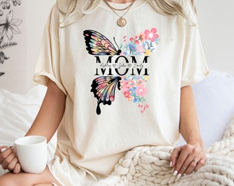 May include: A cream colored t-shirt with a butterfly and floral design. The text "MOM" is centered on the shirt with the names "Ashley", "John", and "Emily" written below.