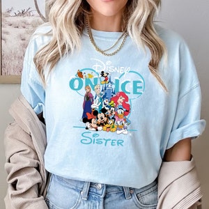 May include: Light blue t-shirt with a graphic of Disney characters on ice, including Mickey Mouse, Minnie Mouse, Donald Duck, Goofy, and others. The text "Disney On Ice Sister" is printed on the shirt.