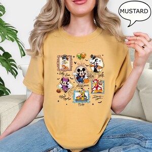 Puede incluir: Camiseta de color mostaza con un dise&ntilde;o tem&aacute;tico de Halloween que presenta im&aacute;genes enmarcadas de personajes de Disney como Mickey Mouse y Donald Duck. El dise&ntilde;o incluye telara&ntilde;as y el texto "Mickey Mouse".