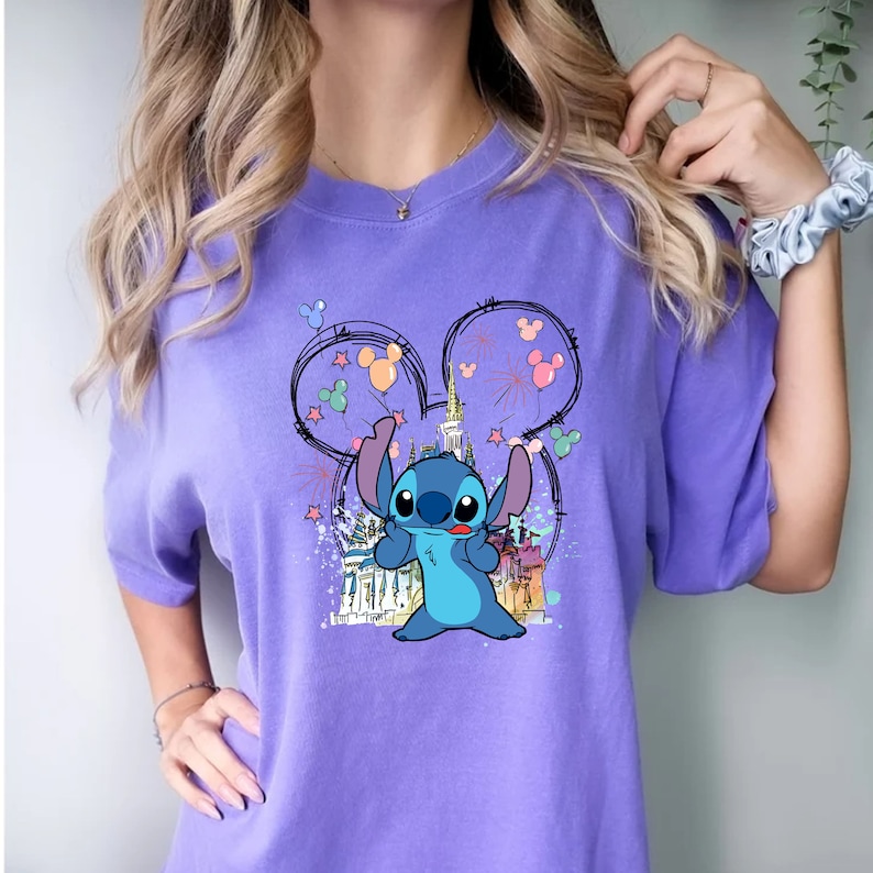 May include: Purple t-shirt with a blue Stitch character holding balloons in front of a cartoon castle. The design is inside a Mickey Mouse ear outline.