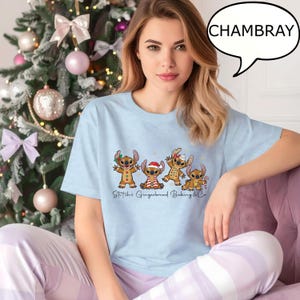 Puede incluir: Camiseta azul claro con un dise&ntilde;o de tem&aacute;tica de pan de jengibre con personajes de dibujos animados. La camiseta tiene el texto "Stitch's Gingerbread Baking & Co." y la palabra "CHAMBRAY" en un bocadillo. La camiseta se usa con pantalones de pijama lilas.