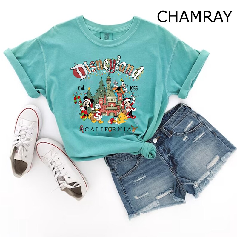 Puede incluir: Una camiseta azul turquesa con un gr&aacute;fico vintage de Disneyland con Mickey Mouse, Donald Duck, Goofy y Pluto. El gr&aacute;fico incluye el texto "Disneyland" con "Est. 1955" y "California" debajo.