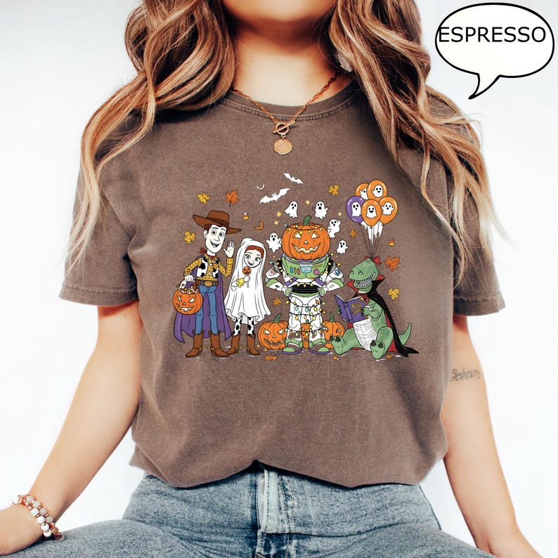 Puede incluir: Camiseta color espresso con un gr&aacute;fico de dibujos animados con tem&aacute;tica de Halloween. El dise&ntilde;o incluye personajes disfrazados de Woody, un fantasma, Buzz Lightyear con cabeza de calabaza y un dinosaurio leyendo un libro, con calabazas y hojas de oto&ntilde;o.