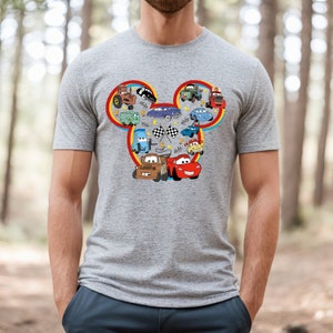 Puede incluir: Una camiseta gris con una silueta de Mickey Mouse formada por varios personajes de Cars. Los personajes incluyen a Mater, Rayo McQueen y otros veh&iacute;culos de la pel&iacute;cula de Disney Pixar.
