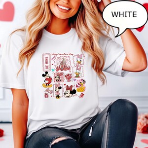 May include: White t-shirt featuring a colorful graphic design with Disney characters and the text "Happy Valentine's Day 2020" and "Be Mine". The design includes Mickey and Minnie Mouse, Daisy Duck, and other characters.
