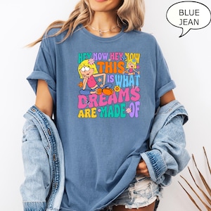 Może przedstawiać: Koszulka z niebieskiego dżinsu z kresk&oacute;wkową grafiką dw&oacute;ch dziewczynek i tekstem "Hey Now Hey Now This Is What Dreams Are Made Of".