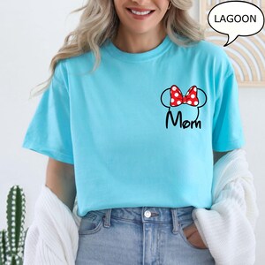 May include: A light blue t-shirt with a red and white polka dot bow and black mouse ears design. The word "Mom" is printed in black below the design. The word "Lagoon" is in a speech bubble.