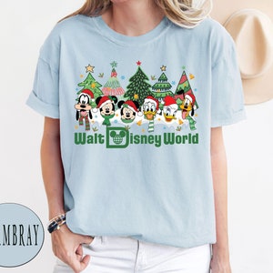 May include: Light blue t-shirt with a Christmas-themed design featuring Mickey Mouse, Minnie Mouse, Donald Duck, Goofy, and Pluto. The design includes Christmas trees, ornaments, and the text "Walt Disney World".