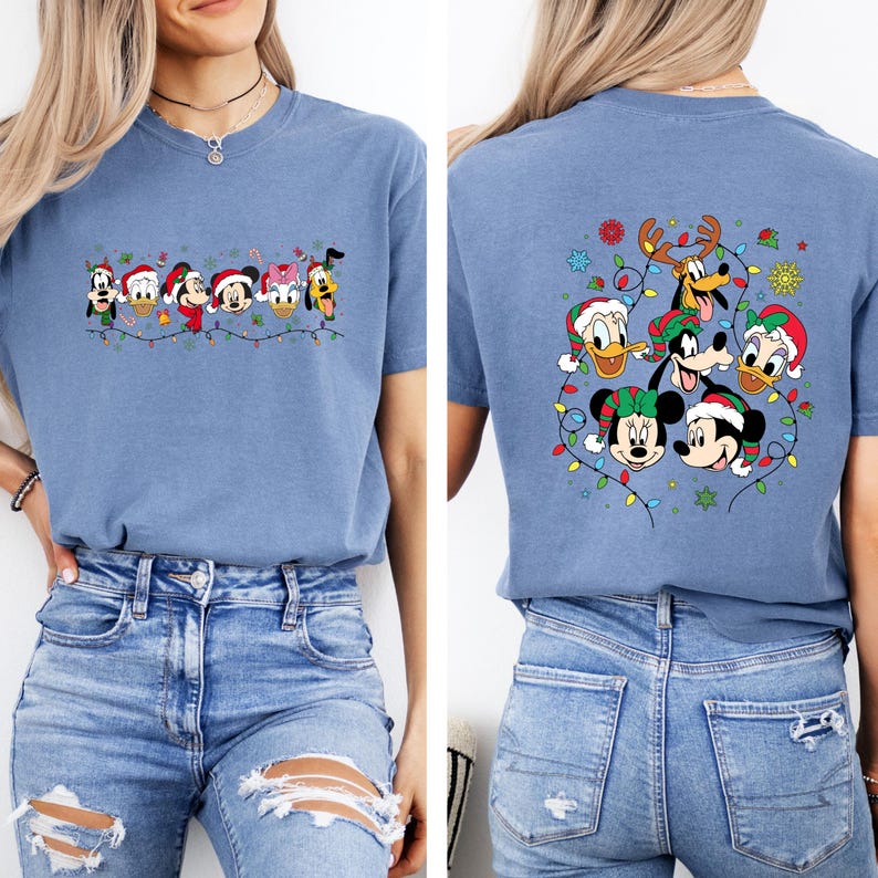 May include: A light blue t-shirt featuring a festive design with Disney characters wearing Santa hats and Christmas lights. The front of the shirt displays a line of characters, while the back showcases a group of characters surrounded by lights and snowflakes.