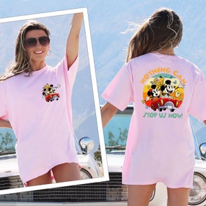 以下が含まれることがあります： 赤い車に乗ったミッキーマウス、ミニーマウス、プルートのグラフィックがプリントされたピンクのオーバーサイズTシャツ。シャツのテキストは「Nothing Can Stop Us Now!」です。