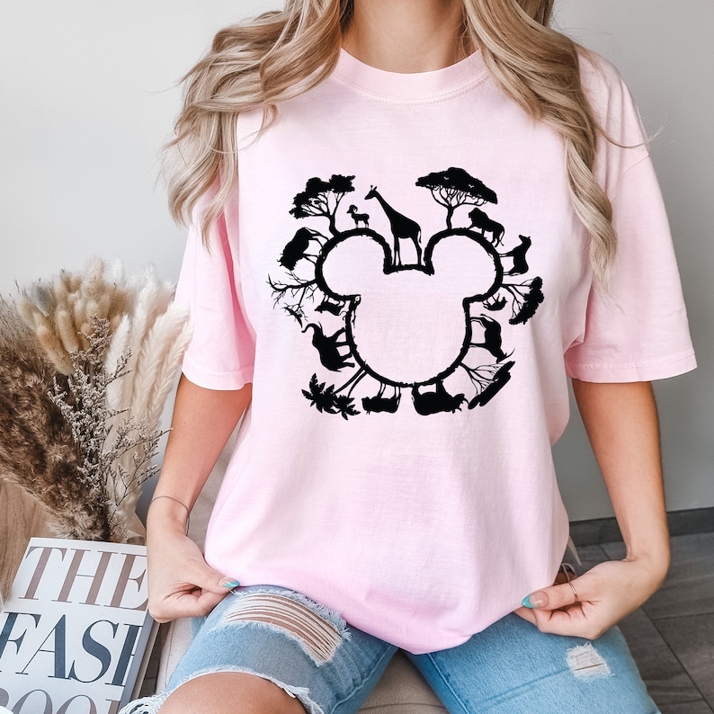 Puede incluir: Una camiseta rosa con una silueta negra de la cabeza de Mickey Mouse. La silueta est&aacute; llena de varios animales y &aacute;rboles, formando un c&iacute;rculo alrededor de la cabeza.