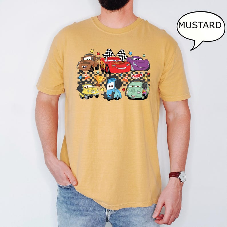 May include: A mustard yellow t-shirt with a cartoon graphic of a group of cars from the Disney Pixar movie Cars. The cars are on a checkered flag background with stars.