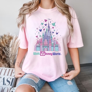 May include: A pink t-shirt with a graphic of Cinderella's castle with pastel colored balloons and the text "Walt Disney World".