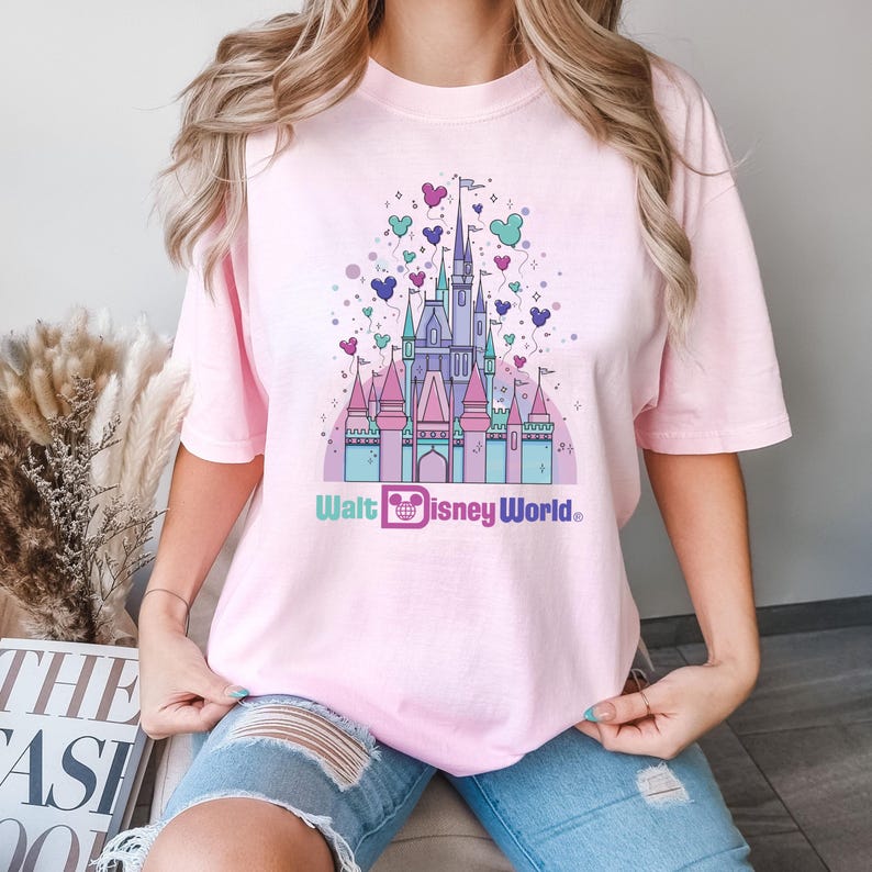 May include: A pink t-shirt with a graphic of Cinderella's castle with pastel colored balloons and the text "Walt Disney World".