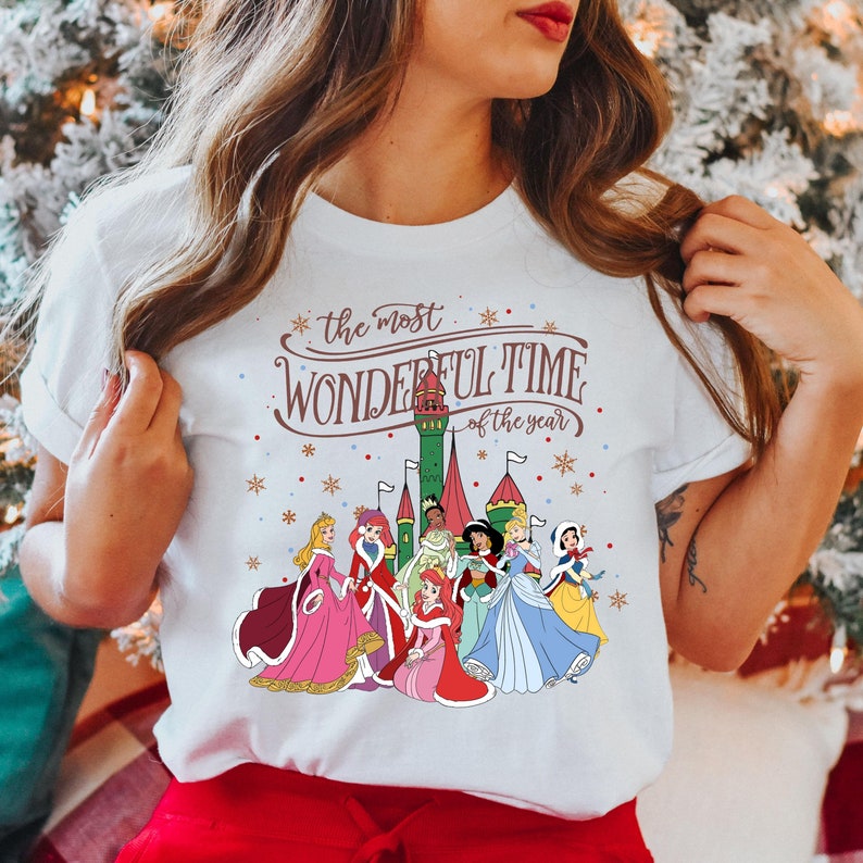 May include: White t-shirt with a Christmas-themed design featuring Disney princesses in front of a castle. The text reads "the most wonderful time of the year".