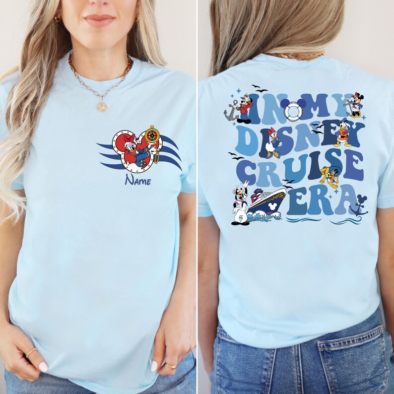 Op de afbeelding: Lichtblauw T-shirt met een Mickey Mouse-ontwerp aan de voorkant en de tekst "In My Disney Cruise Era" met Disney-figuren op de achterkant.