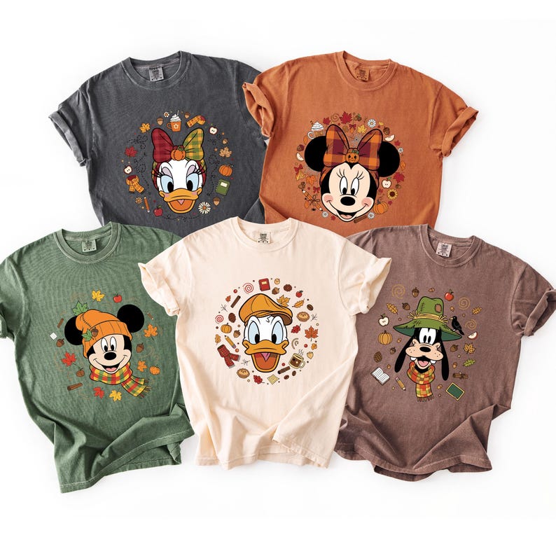 May include: Five short-sleeved t-shirts in various colors, each featuring a different Disney character in a fall-themed design. Characters include Daisy Duck, Minnie Mouse, Mickey Mouse, Donald Duck, and Goofy, surrounded by autumn leaves and accessories.