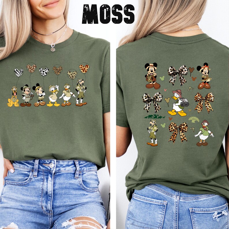 May include: A green t-shirt with a print of Disney characters dressed in safari outfits. The front of the shirt features the characters holding balloons. The back of the shirt features the characters with leopard print bows. The text "MOSS" is printed on the shirt.