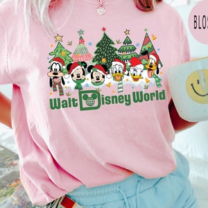 May include: Pink t-shirt with a graphic of Mickey Mouse, Minnie Mouse, Goofy, Donald Duck, and Pluto dressed in Christmas outfits in front of Christmas trees. The text "Walt Disney World" is printed below the characters.
