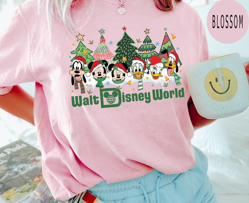 May include: Pink t-shirt with a graphic of Mickey Mouse, Minnie Mouse, Goofy, Donald Duck, and Pluto dressed in Christmas outfits in front of Christmas trees. The text "Walt Disney World" is printed below the characters.
