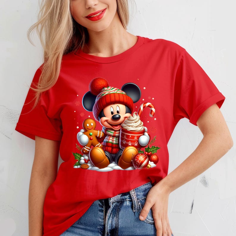 Puede incluir: Camiseta roja con un gr&aacute;fico navide&ntilde;o con Mickey Mouse con un gorro y una bufanda rojos y verdes, sosteniendo una taza de chocolate caliente y un hombre de jengibre.
