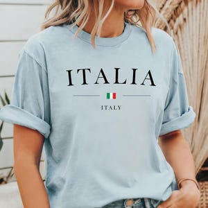 May include: Light blue t-shirt with the word "ITALIA" and the Italian flag printed on the front. The text "ITALY" is printed below the flag.