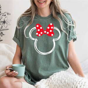 May include: A green t-shirt with a white outline of Mickey Mouse's head and a red bow with white polka dots.