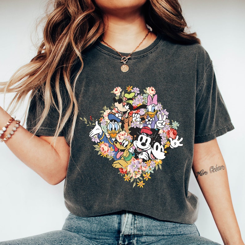 May include: A dark grey t-shirt featuring a graphic print of Mickey Mouse and his friends surrounded by colourful flowers. The shirt has a cropped fit and short sleeves.