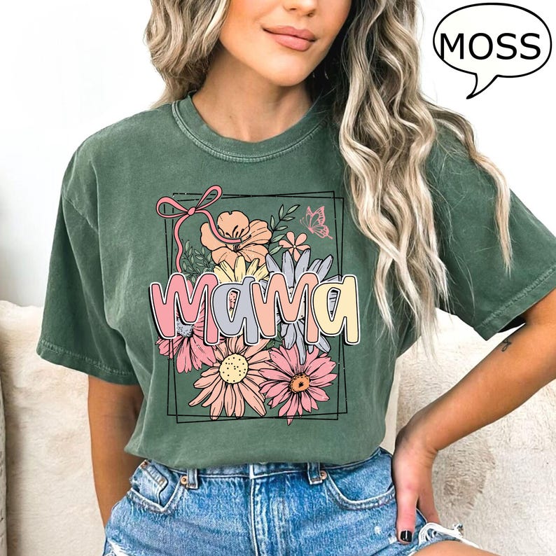May include: Green t-shirt with a floral design and the word "mama" in colorful letters. The design is framed by a black rectangle.