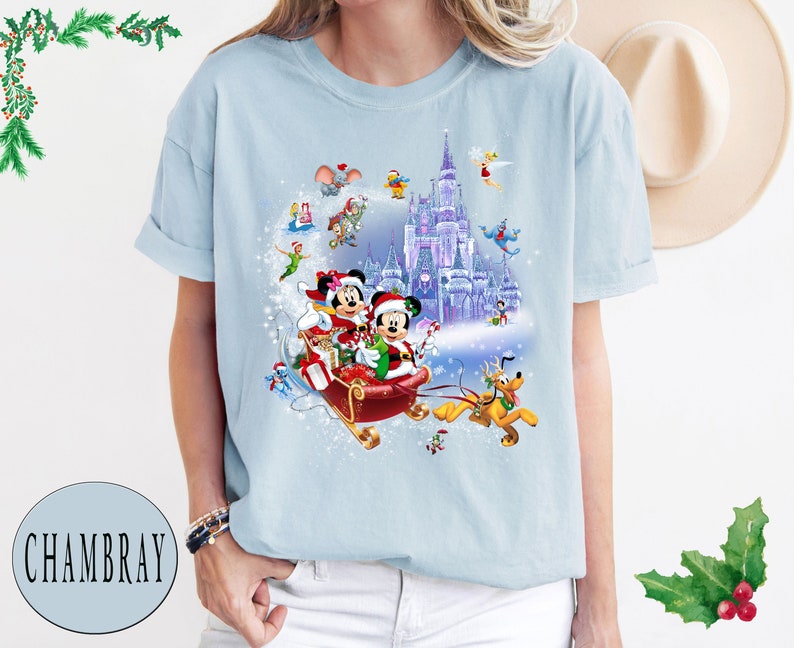 Puede incluir: Una camiseta azul claro con un dise&ntilde;o navide&ntilde;o que presenta a Mickey Mouse y Minnie Mouse en un trineo tirado por Pluto. El dise&ntilde;o tambi&eacute;n incluye el castillo de Cenicienta y otros personajes de Disney.