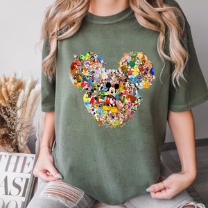 May include: A green t-shirt with a large Mickey Mouse head design. The design is made up of many different Disney characters, including Mickey Mouse, Minnie Mouse, Donald Duck, Goofy, and Pluto.