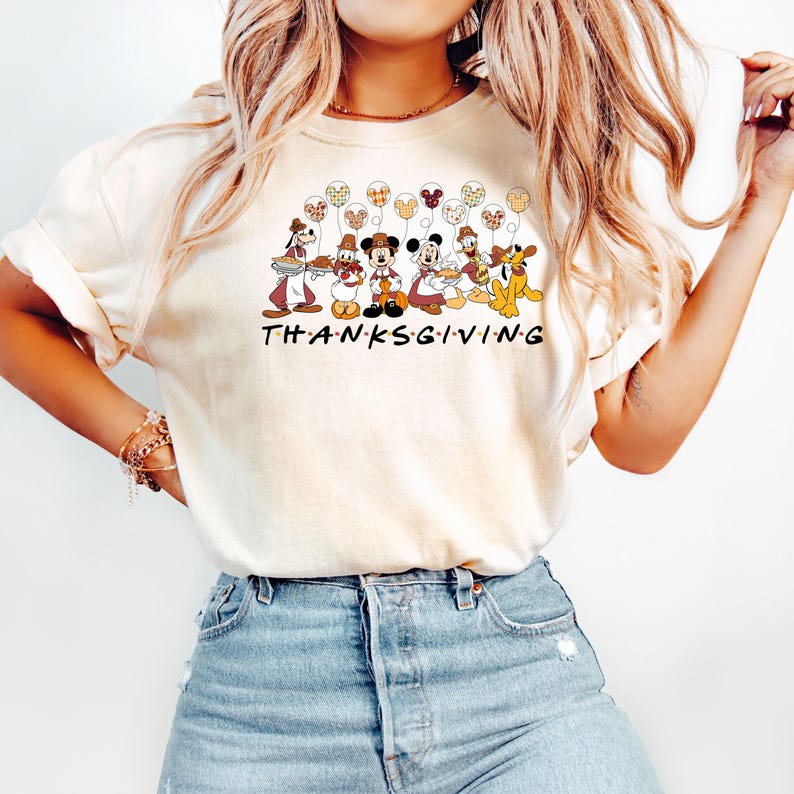 May include: A white t-shirt with a graphic of Mickey Mouse and friends dressed in Thanksgiving costumes. The graphic includes the text "THANKSGIVING".