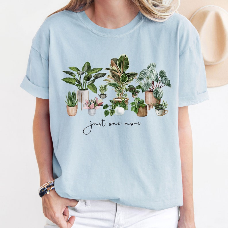 May include: Light blue t-shirt with a watercolor illustration of potted plants and the text "just one more".