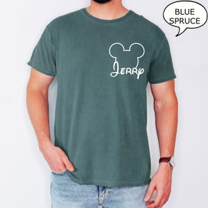 May include: A blue spruce t-shirt with a white Mickey Mouse head outline and the name "Jerry" in a script font. The shirt is a solid color and has a classic crew neck design.