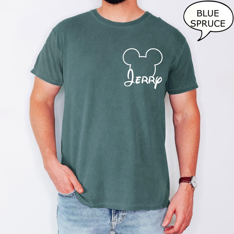 May include: A blue spruce t-shirt with a white Mickey Mouse head outline and the name "Jerry" in a script font. The shirt is a solid color and has a classic crew neck design.