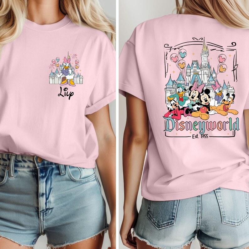 May include: Pink t-shirt with a graphic of Disney characters in front of the Cinderella Castle. The back of the shirt has a graphic of Mickey Mouse, Minnie Mouse, Donald Duck, Goofy, Pluto, and Daisy Duck in front of the Cinderella Castle with the text "Disneyworld - Est. 1955".