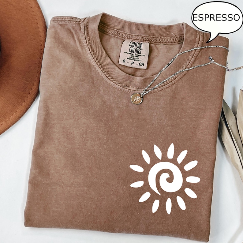 May include: A brown t-shirt with a white sun graphic and the text "COMFORT COLORS" on the tag. The shirt is labeled "ESPRESSO".