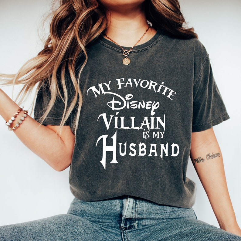 Pu&ograve; includere: Una maglietta grigia con la scritta "My Favorite Disney Villain is My Husband" stampata in bianco.