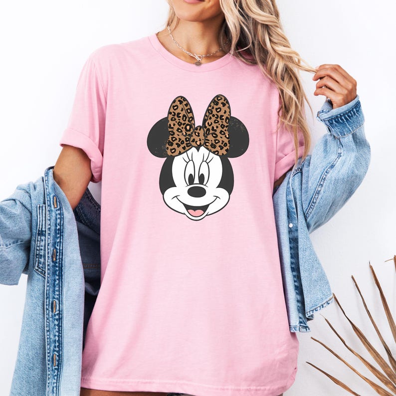 May include: Pink t-shirt with a cartoon image of Minnie Mouse wearing a leopard print bow.