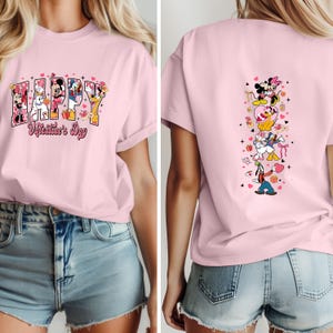 May include: A light pink t-shirt featuring the word "HAPPY" with Disney characters and the text "Valentine's Day". The back of the shirt has a vertical design with more Disney characters and hearts.