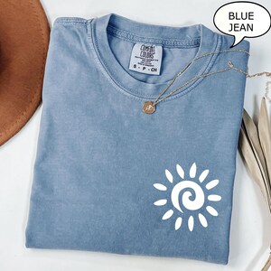 May include: A blue jean t-shirt with a white sun graphic. The shirt has a tag that says "Comfort Colors" and "S-P-CH".
