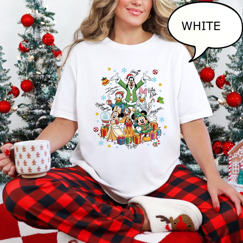 Puede incluir: Camiseta blanca con un dise&ntilde;o gr&aacute;fico colorido de personajes de Disney, incluyendo Mickey y Minnie Mouse, Donald Duck y Goofy, rodeados de regalos y copos de nieve. La palabra "WHITE" est&aacute; en una burbuja.