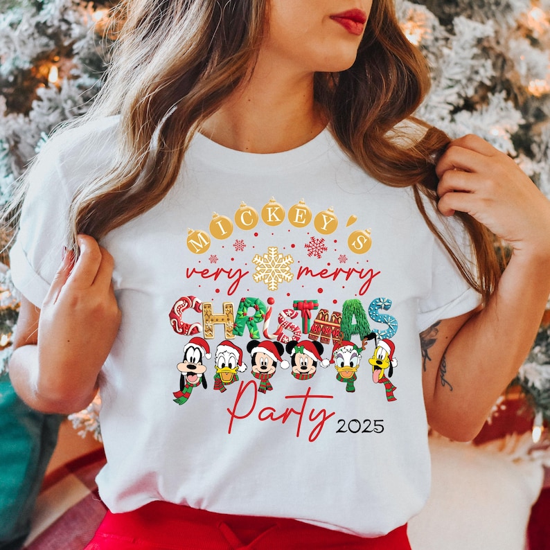K&ouml;nnte beinhalten: Wei&szlig;es T-Shirt mit einem Mickey Mouse Weihnachtsparty-Design. Das Design zeigt Mickey Mouse, Minnie Mouse, Donald Duck, Goofy und Pluto, die Weihnachtsm&uuml;tzen und Weihnachtspullover tragen. Der Text auf dem Shirt lautet "Mickey's very merry Christmas Party 2025".