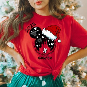 Peut inclure: T-shirt rouge avec une silhouette noire de Mickey Mouse portant un bonnet de P&egrave;re No&euml;l. La silhouette comprend des feux d'artifice, un ch&acirc;teau et le texte "Making Disney Memories 2025" et "Disney Sister".