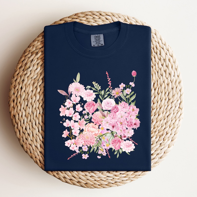 Puede incluir: Una camiseta azul marino con un estampado floral rosa. El estampado presenta una variedad de flores, incluyendo rosas, peon&iacute;as y flores de cerezo.